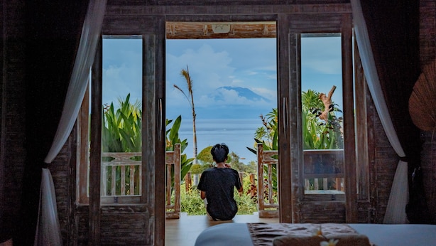 A person sitting by a large window with a view of a mountain and plants. - Gara Gara Sea View (Penida Island)