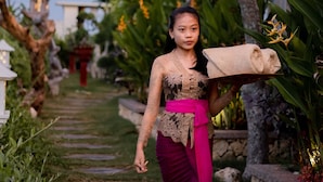 A person walking on a stone pathway in a garden with tropical plants and a traditional building with a red roof. - Gara Gara Sea View (Penida Island)