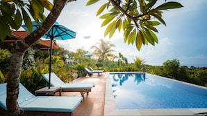 A pool area with lounge chairs and umbrellas, surrounded by tropical vegetation. - Gara Gara Sea View (Penida Island)