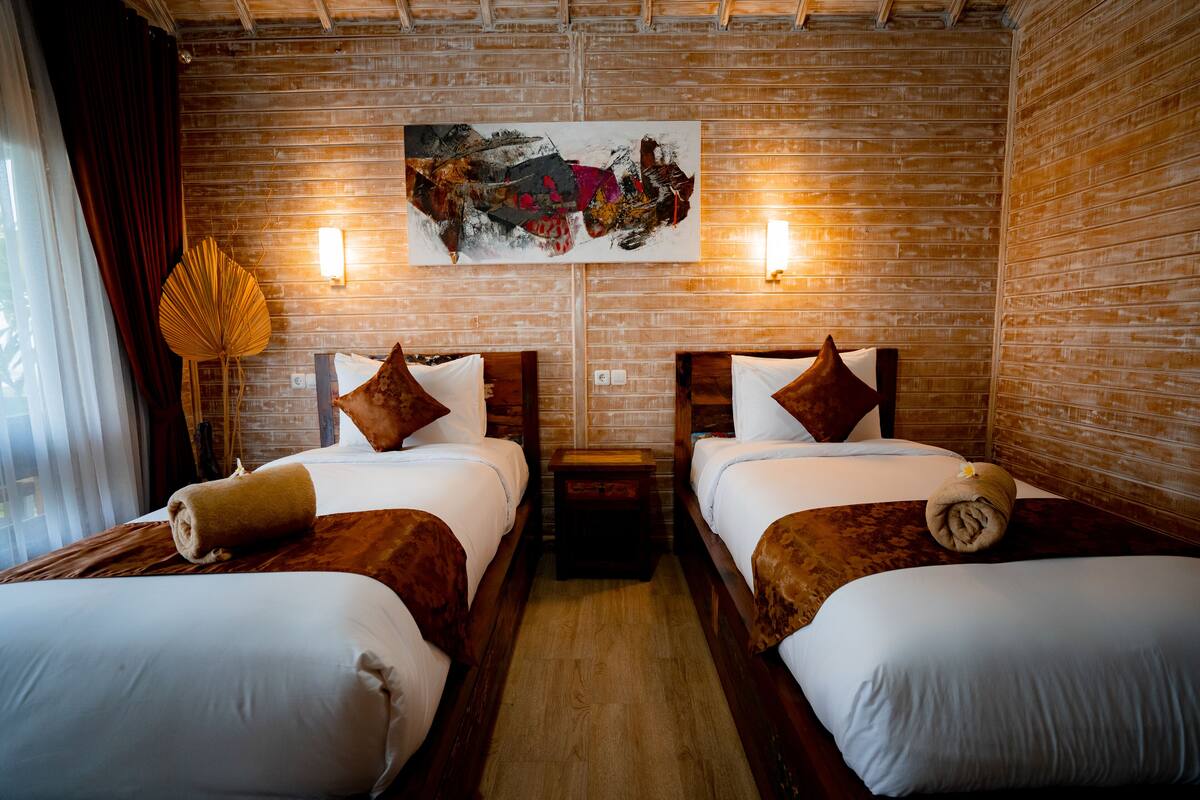 A hotel room with two beds, wooden headboards, a large abstract painting on the wall, and a window with curtains.