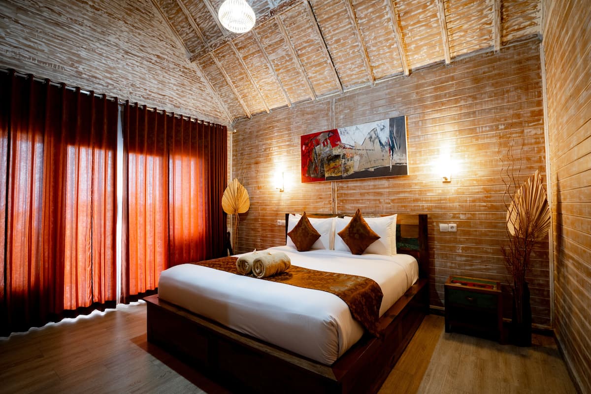 A spacious bedroom with a large bed, wooden ceiling, and a painting on the wall.