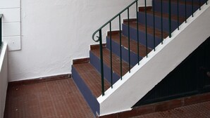 Eine Treppe mit Metallgeländer führt zu einer Tür, ein an der Wand befestigtes Schild mit der Aufschrift „MR MADEIRAROMAS Accommodations“ und eine Leuchte über der Tür.