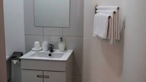 Ein kleines, sauberes Badezimmer mit weißem Waschbecken, Spiegel und Handtuchhalter.