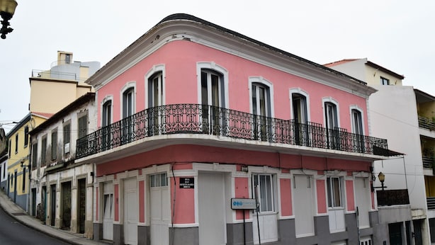 Ein rosafarbenes Gebäude mit Balkon und einem Schild für 'Clinica de Dermatologia', vor der Tür eine Straße.