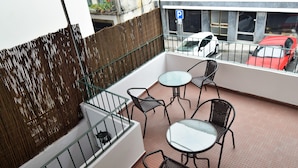 Ein Balkon mit Tisch und Stühlen, Blick auf ein rotes Auto und ein Gebäude mit einem 'P'-Parkplatzschild.