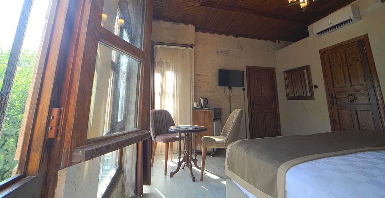 A bedroom with a bed, a chair, a small table, a television, and a wooden door.