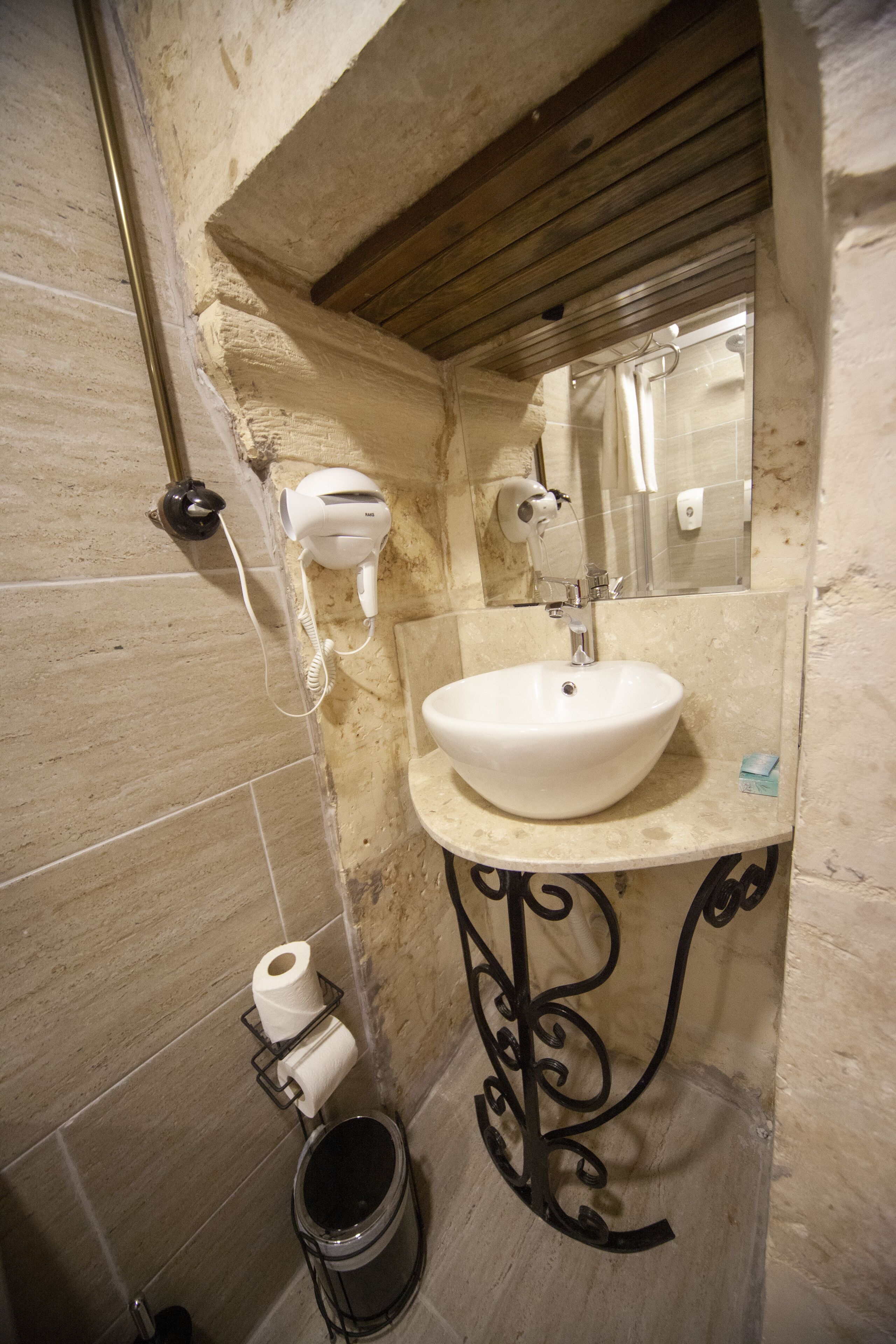 Un bagno con un lavandino bianco, un asciugacapelli, uno specchio e un portasciugamani per carta igienica.