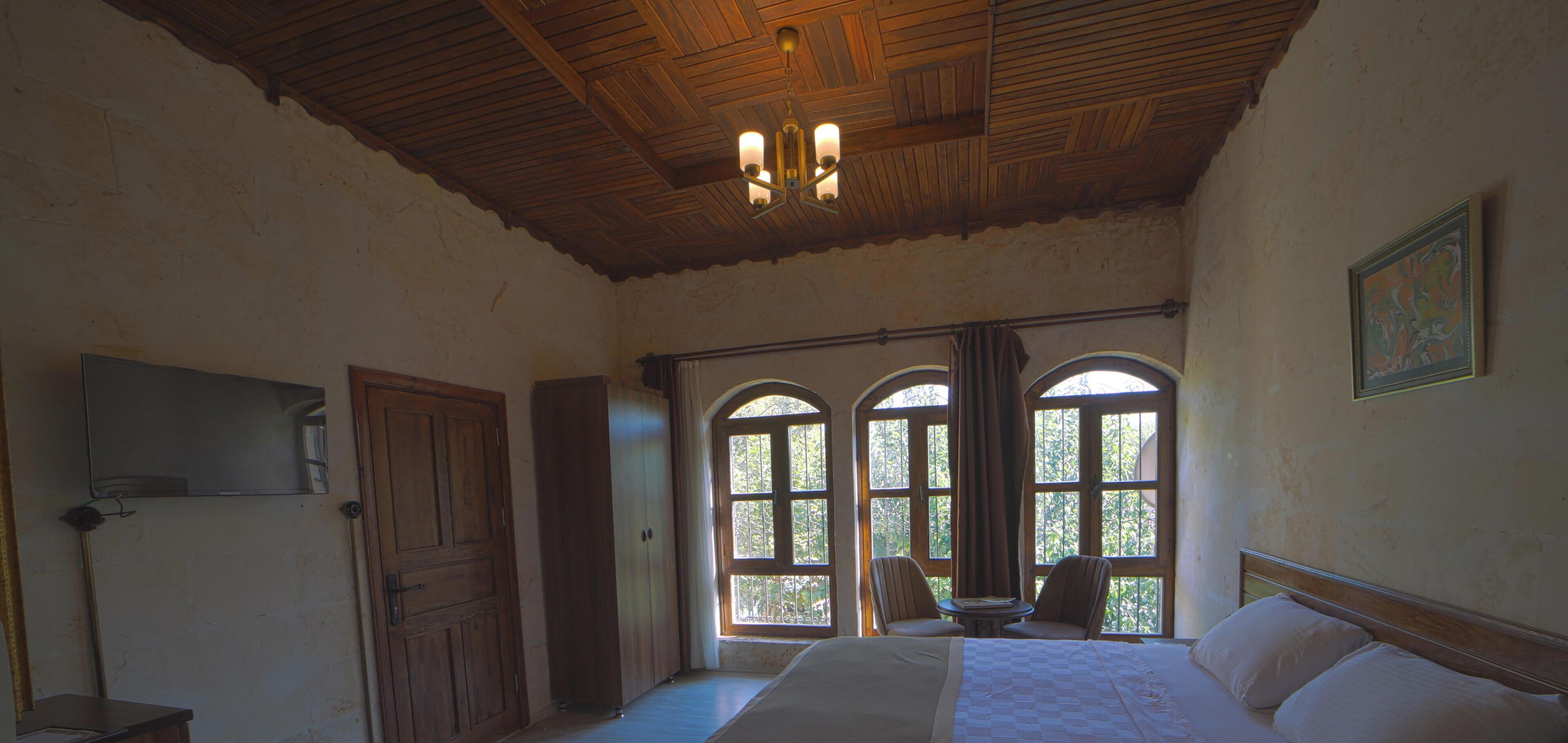 Una habitación de hotel con una cama grande, techo de madera y ventanas arqueadas.