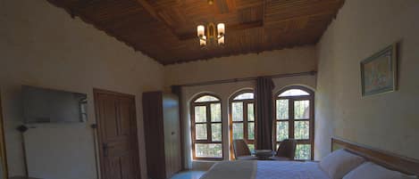 A hotel room with a large bed, wooden ceiling, and arched windows.