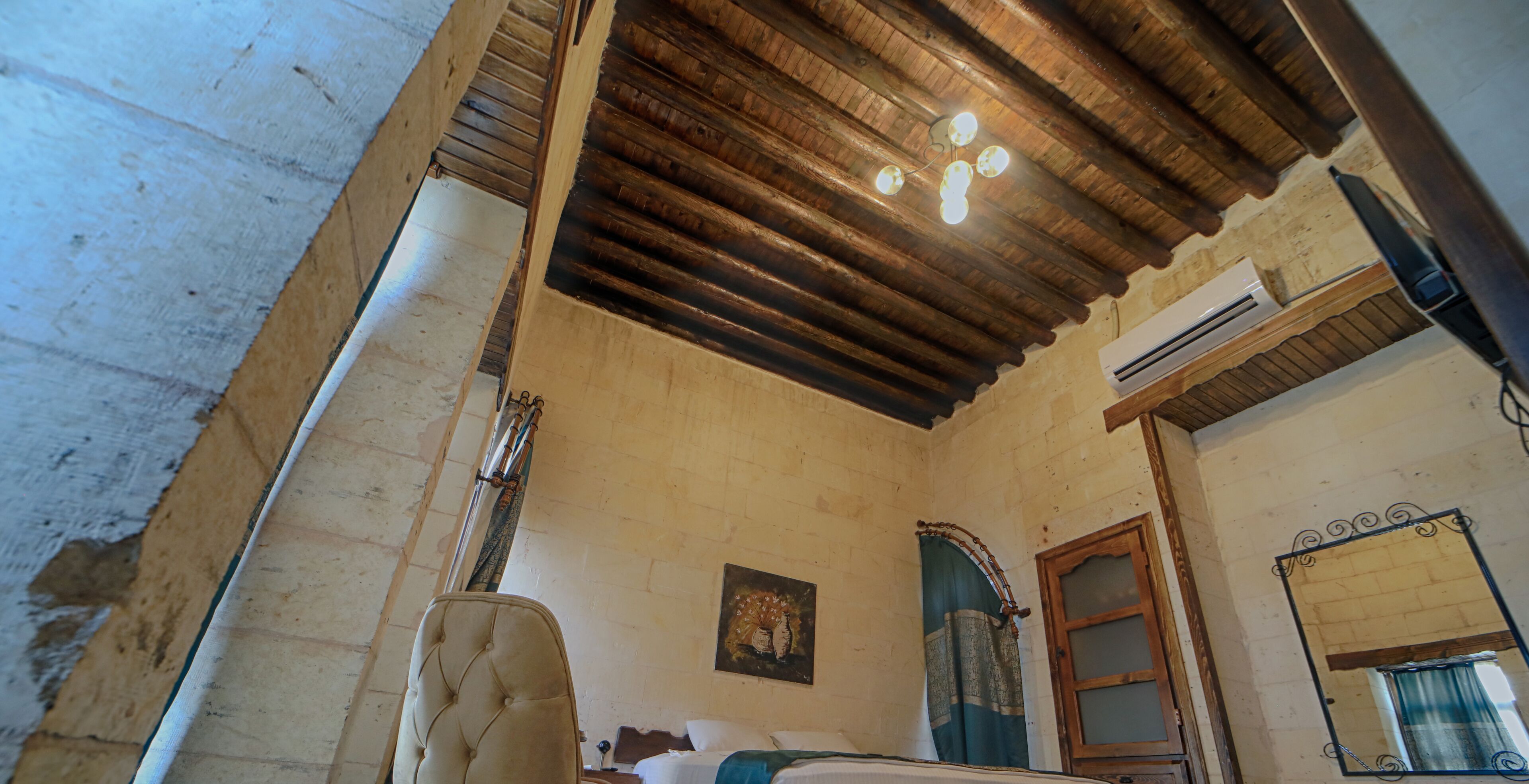 A room with a wooden ceiling, a bed, a wall-mounted air conditioner, and a mirror.