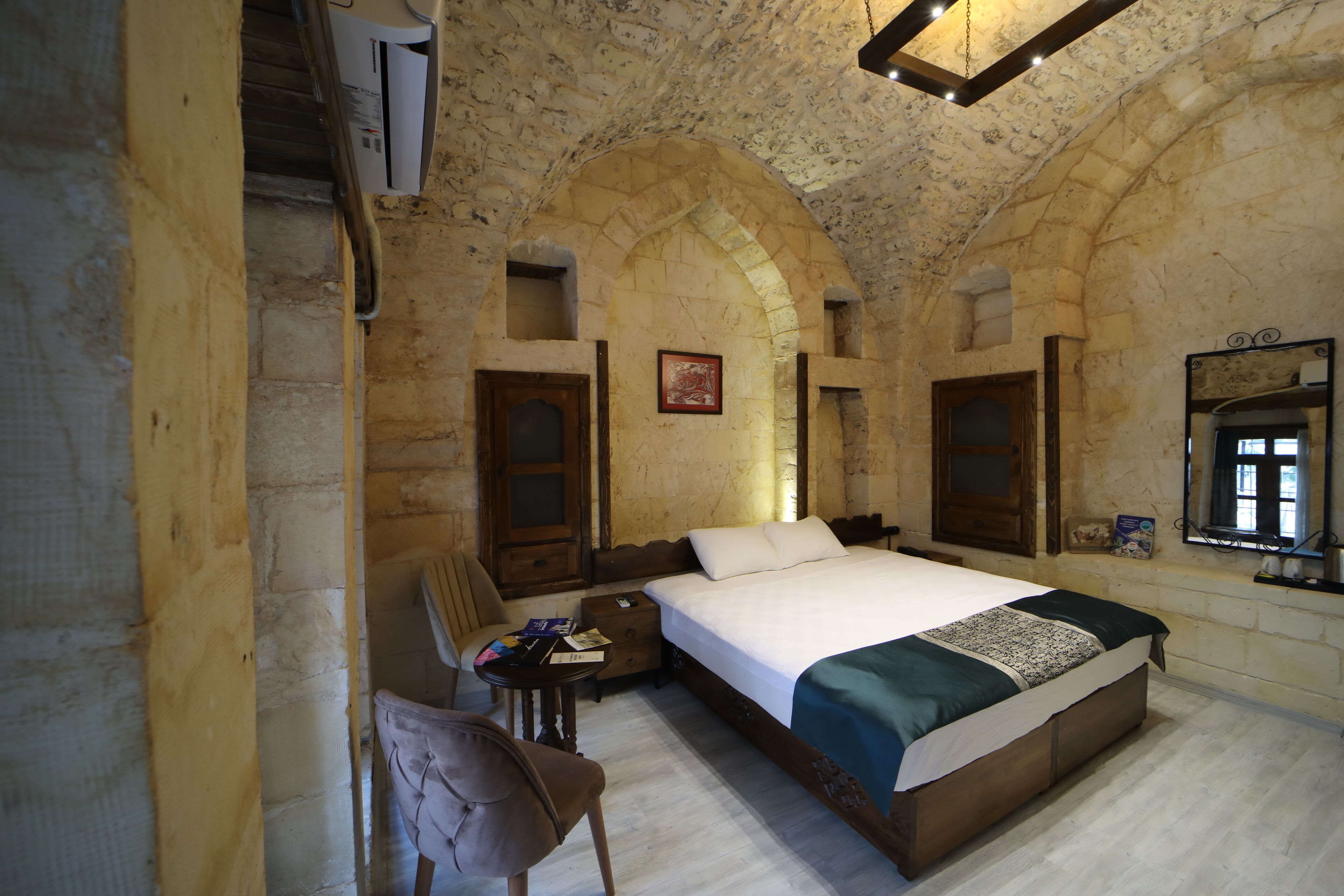 Ein Schlafzimmer mit einem großen Bett, einem Holzstuhl, einem kleinen Tisch und einer Steinwand mit Rundbögen.