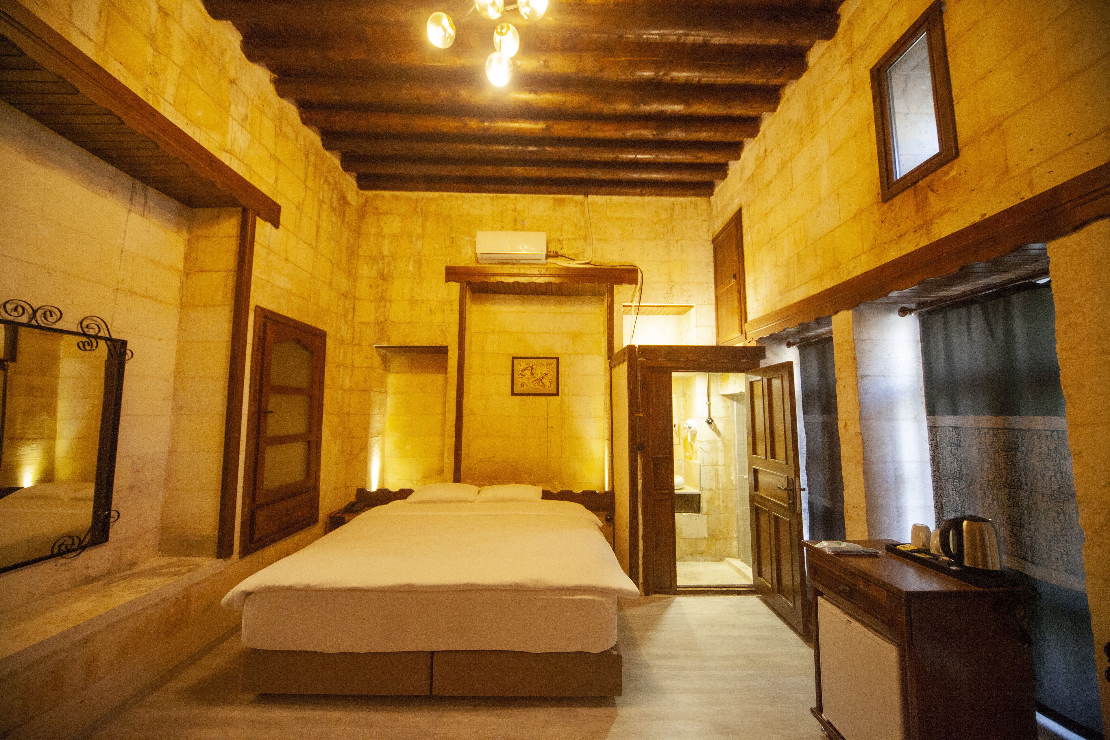 Una habitación con cama, escritorio y hervidor, y puerta que da a otra habitación.