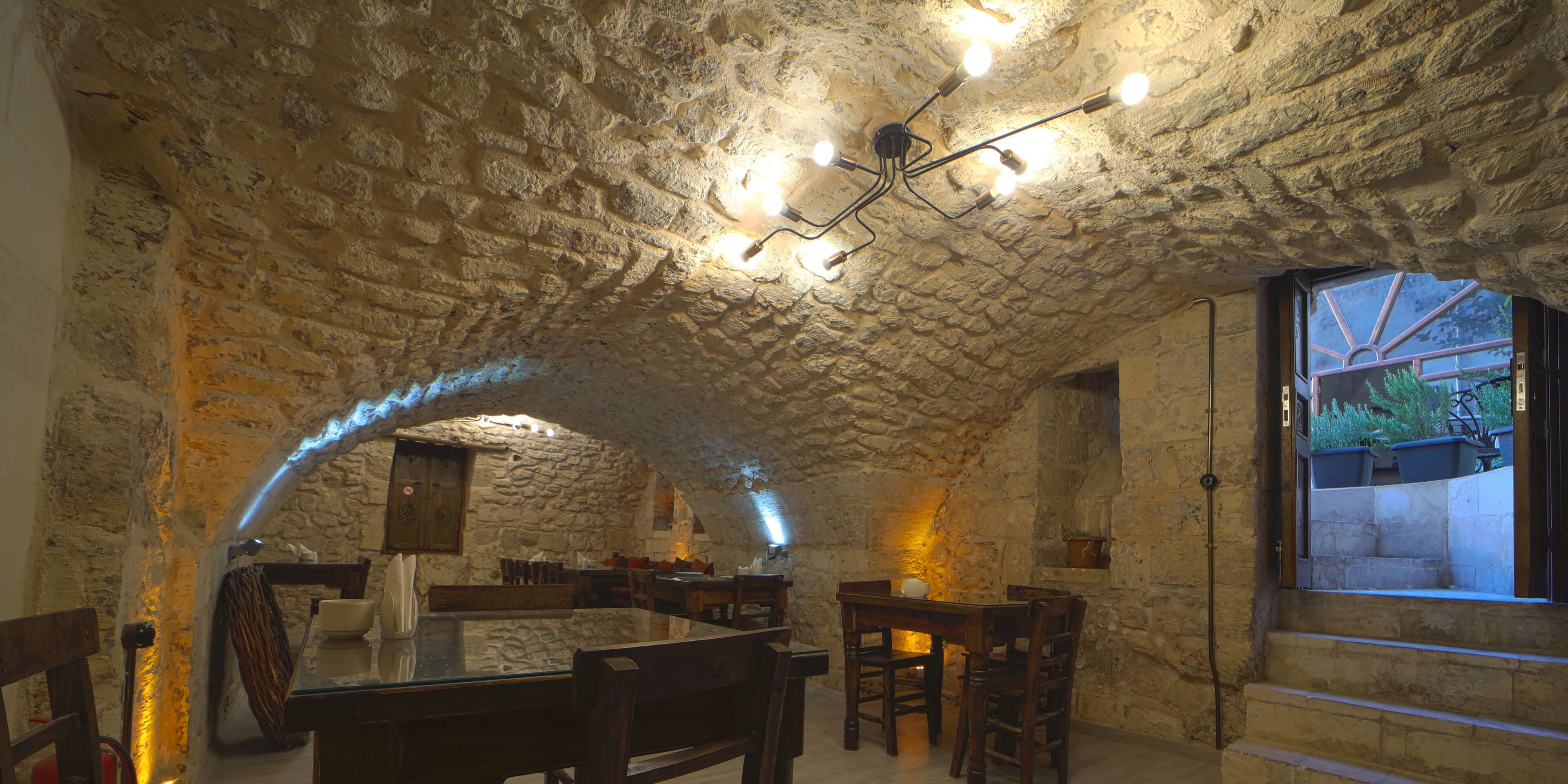 A rustic stone interior with a vaulted ceiling, wooden furniture, and a view through a window.