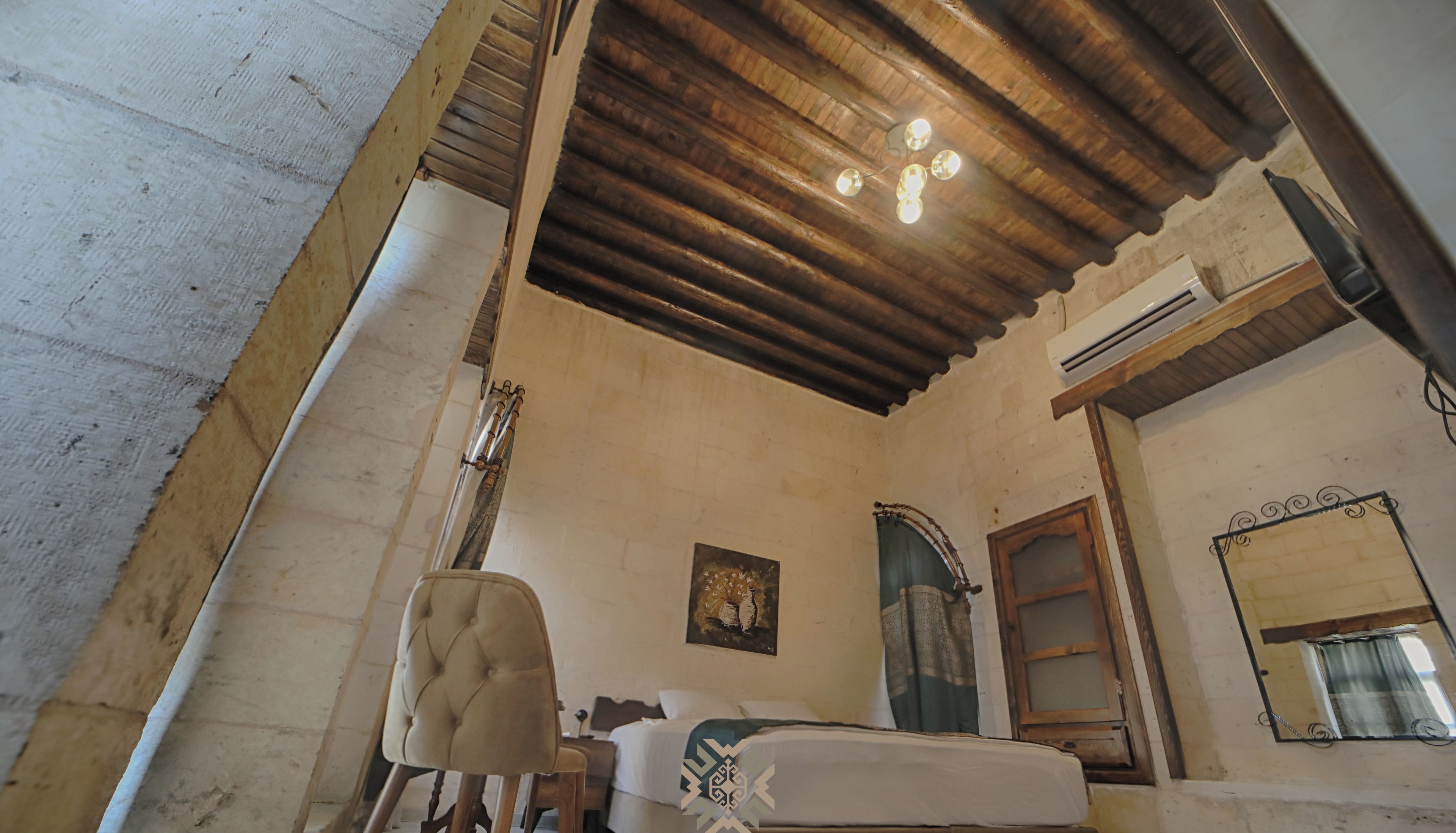 A bedroom with a wooden ceiling, a bed, a chair, a mirror, and an air conditioning unit.