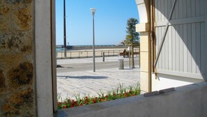Blick auf die Küste durch einen Rundbogen mit einer Steinmauer, einer Straßenlaterne, einer Bank und einem Mülleimer.