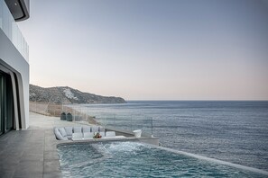 A modern infinity pool with a view of the sea and a mountainous landscape.