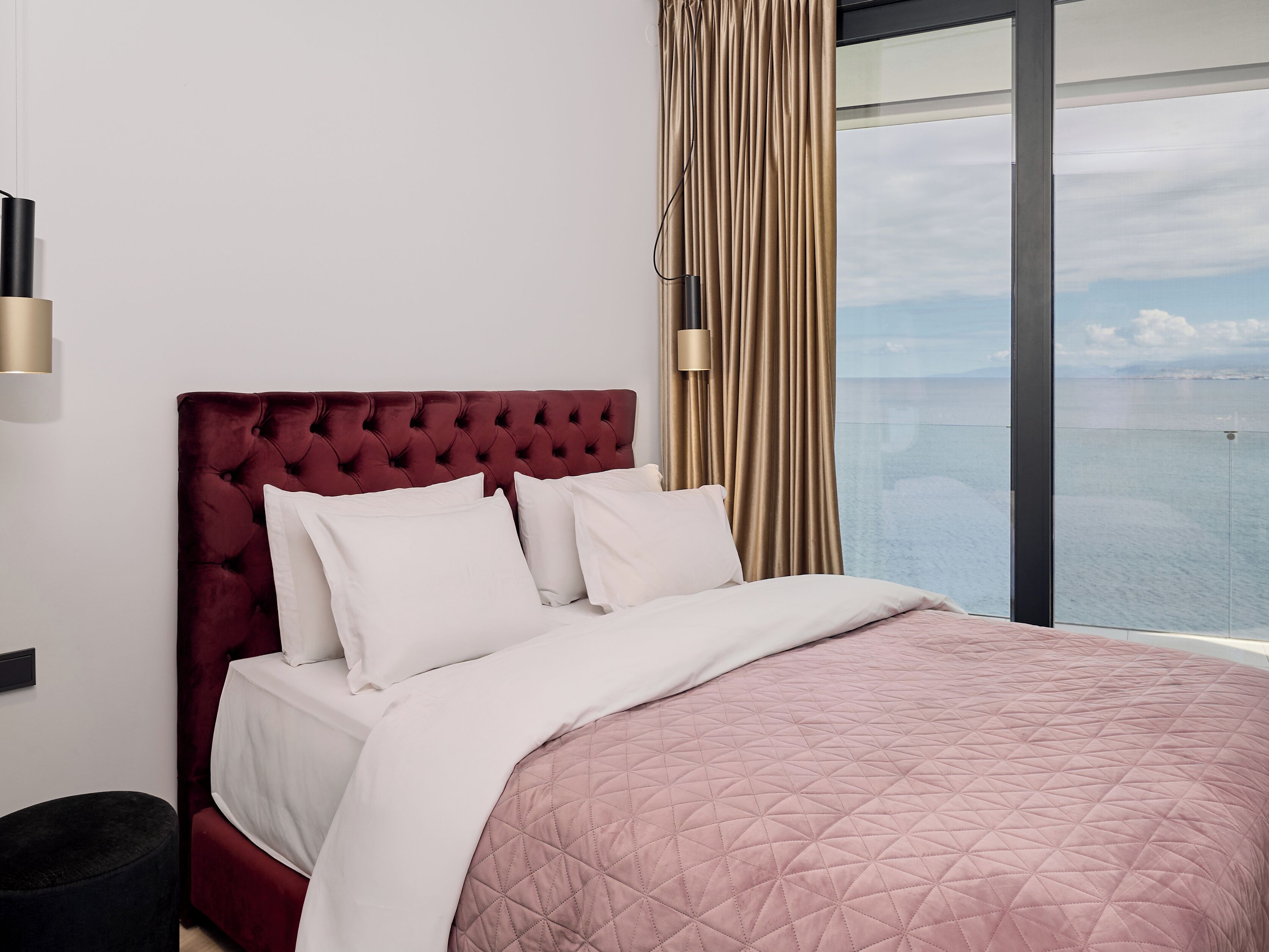 A bed with a tufted headboard, white bedding, and a pink quilted blanket.
