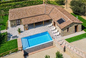 En villa med swimmingpool, udendørs siddepladser og en bygning i sten.