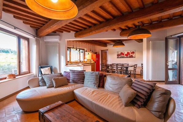 A cozy living room with a large L-shaped sofa, wooden ceiling beams, and pendant lighting. - Villa Il Melograno - Four Bedroom Villa, Sleeps 8 (Parrano)
