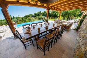 Un área de comedor al aire libre con vista a la piscina, pérgola de madera y muros de piedra.