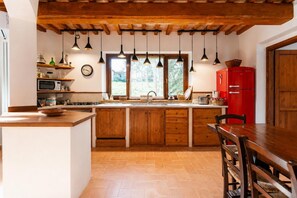 Una cocina con armarios de madera, un refrigerador rojo y lámparas colgantes.