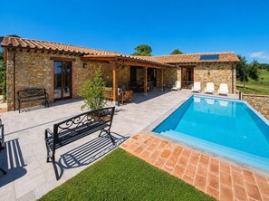 En bygning i sten med swimmingpool, udendørs møbler og et pergola-tag.