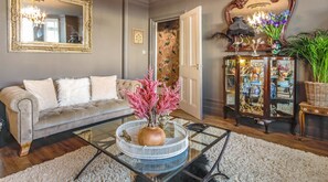 A living room with a beige sofa, a glass coffee table with pink decorative plants, and a decorative cabinet with glass doors.