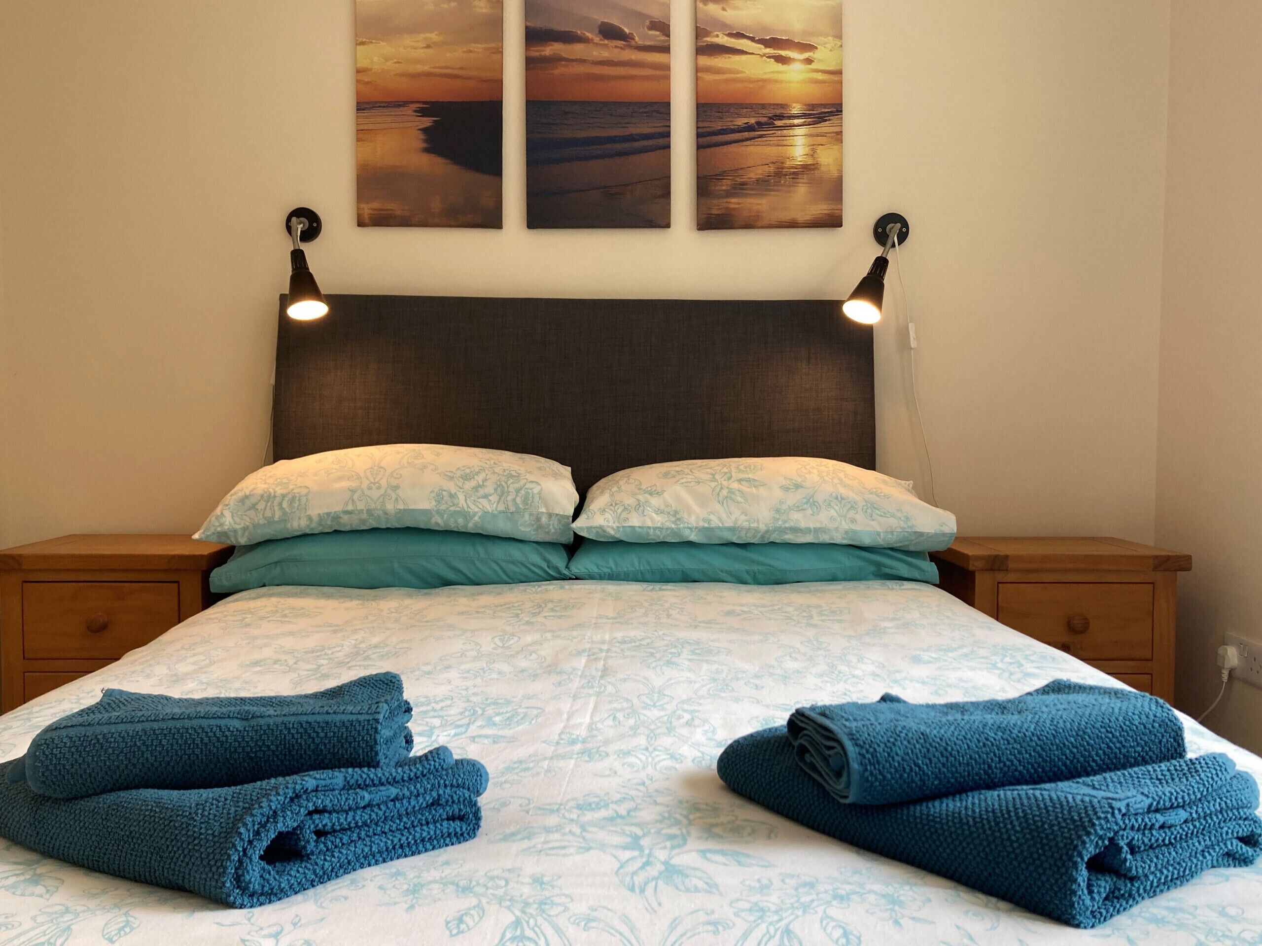 A bed with a patterned bedspread, two pillows, and two rolled towels.
