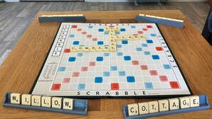 Un joc de Scrabble damunt un taulell de fusta, amb les peces i els marcadors de puntuació.
