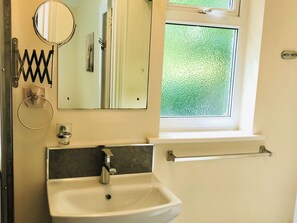 A bathroom with a sink, mirror, towel ring, and window. - Creekside Cottage (Wootton Bridge)