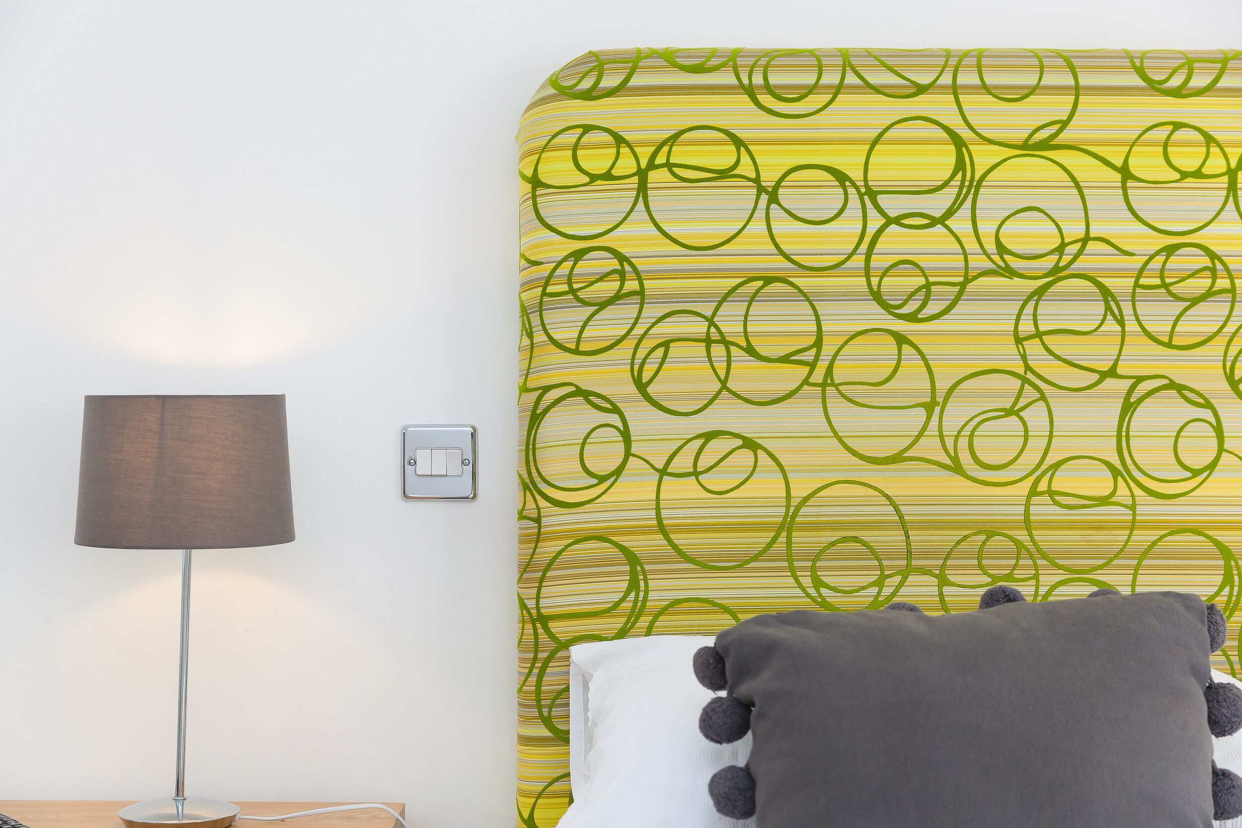 A room with a bed, a lamp, and a wall with a green and yellow pattern.