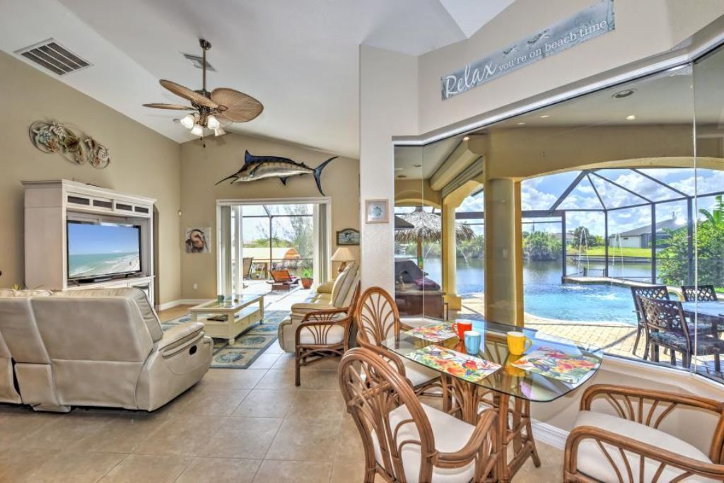 A spacious living area with a large TV, comfortable seating, and a glass door leading to a pool.