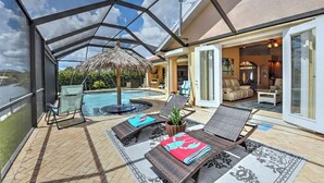 Un espacio exterior techado con piscina, sillas de descanso y un parasol de paja.