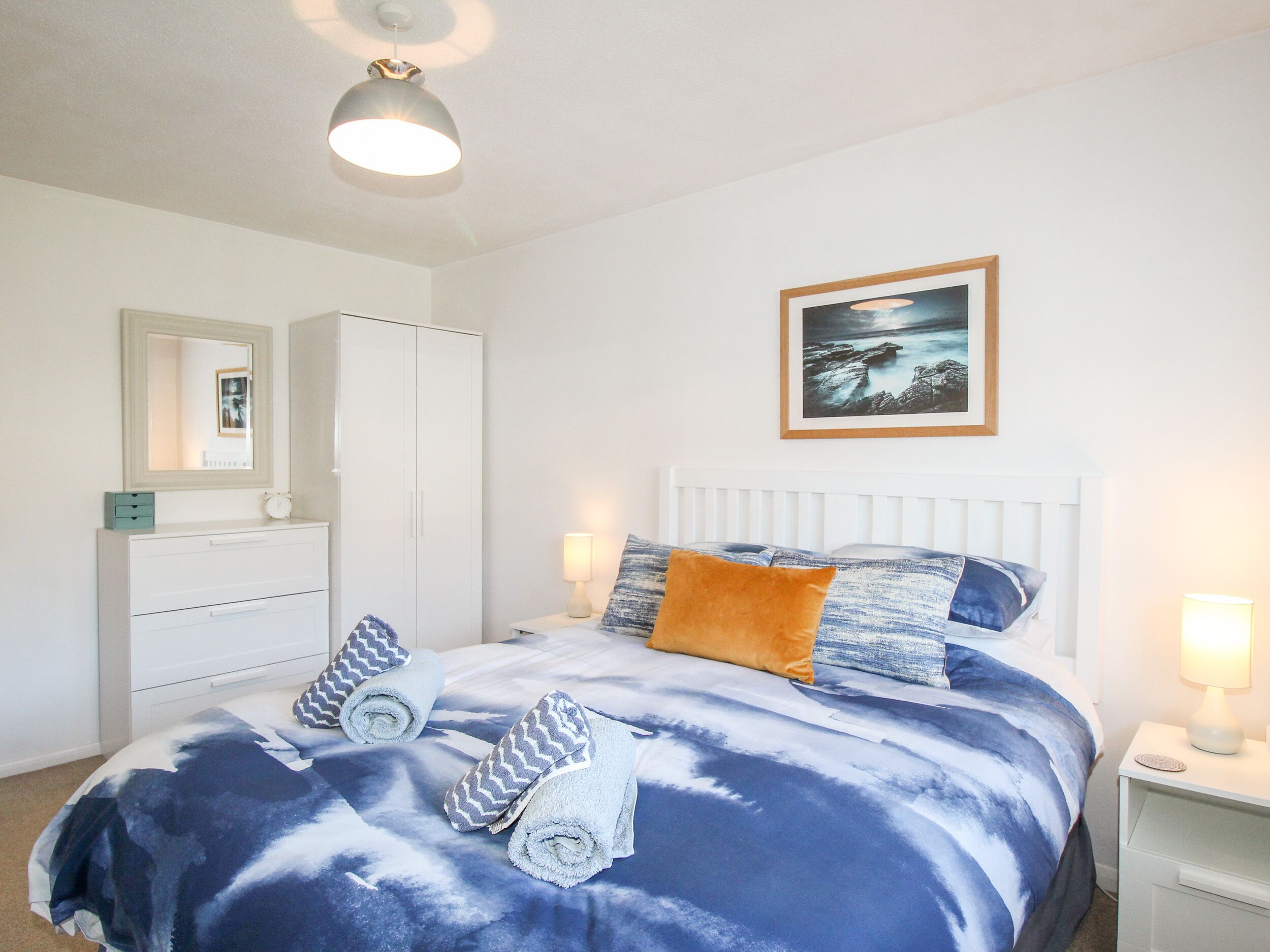A bedroom with a bed, a wardrobe, a bedside table, a lamp, and a framed picture on the wall.