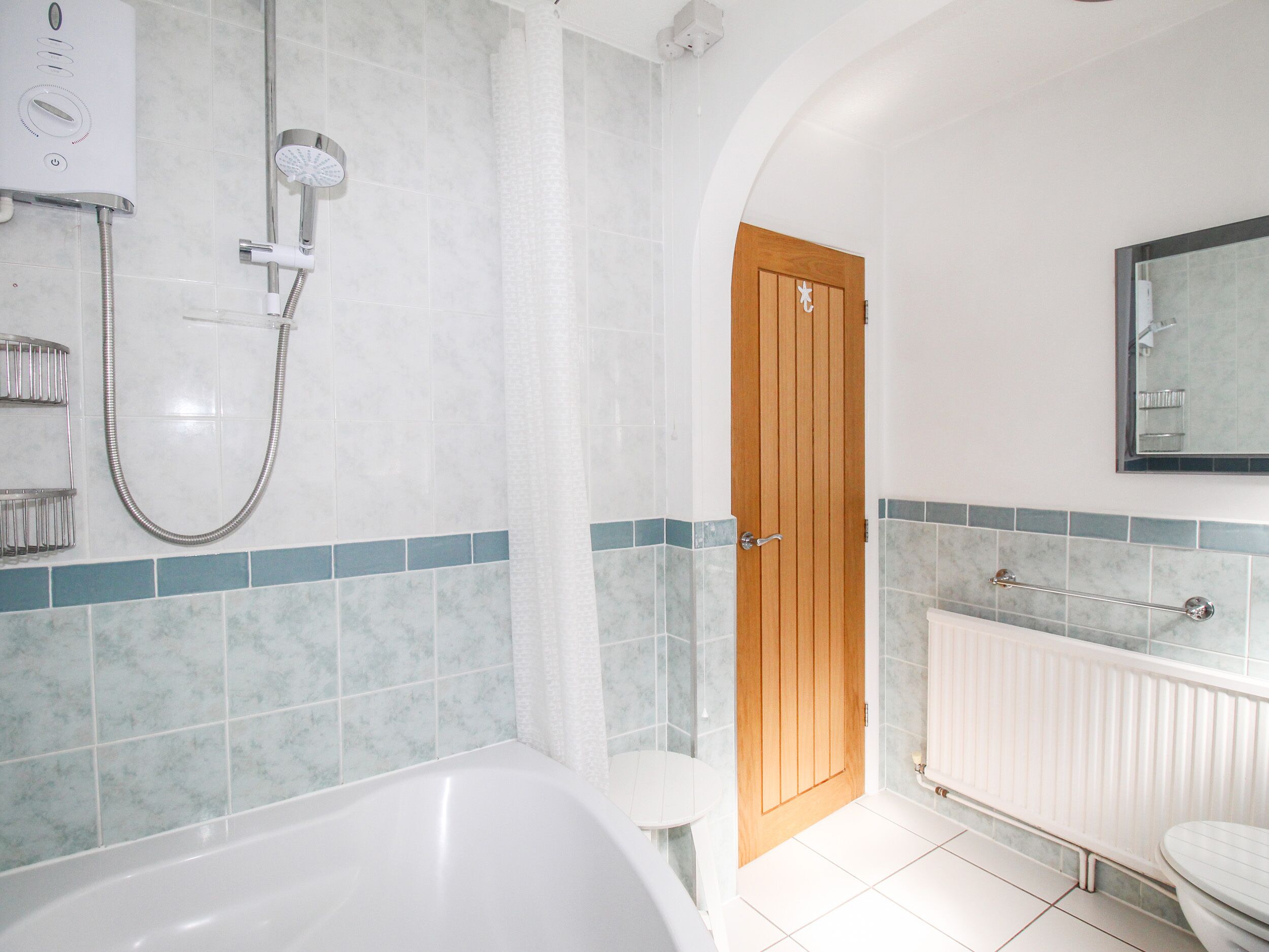 A bathroom with a bathtub, a shower, a toilet, and a wooden door.