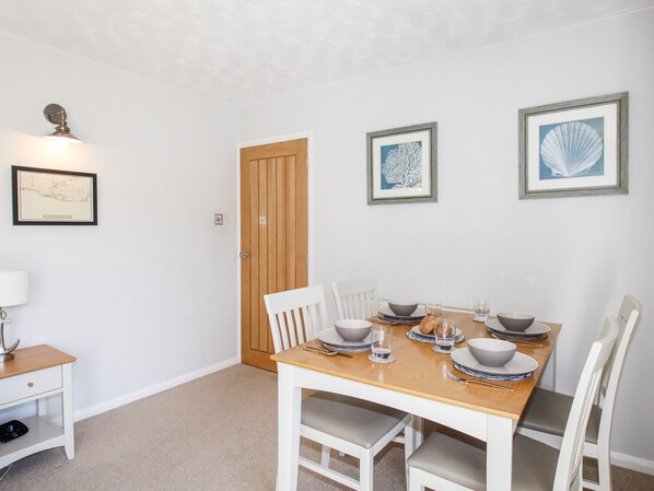 A dining room with a wooden table set for four, white chairs, and framed artwork on the walls.