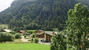 Uma pousada na montanha com vários edifícios, rodeada por vegetação exuberante e uma paisagem montanhosa arborizada.