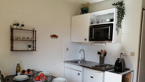 Uma cozinha compacta com micro-ondas, pia e uma pequena geladeira. Há uma mesa de jantar posta com pratos, copos e uma garrafa.