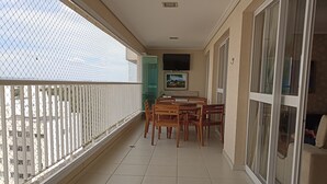A balcony with a tiled floor, a table with chairs, a painting on the wall, and a sliding glass door. - Gorgeous appartement in condominium club (São José dos Campos)