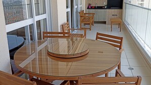 A spacious balcony with a round glass table and wooden chairs, a kitchen area with patterned cabinets, and a view of the cityscape. - Gorgeous appartement in condominium club (São José dos Campos)