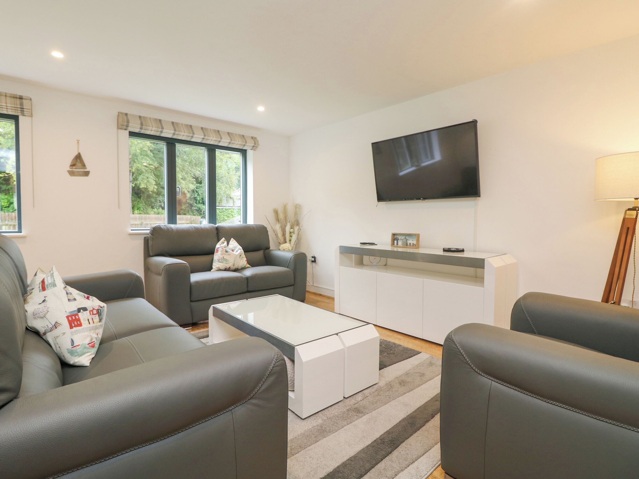 A modern living room with a grey sofa set, a white coffee table, and a flat-screen TV mounted on the wall.