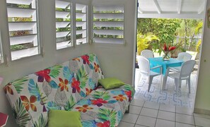 Ein Zimmer mit einer Couch, einem Tisch, Stühlen und Blick ins Grüne.