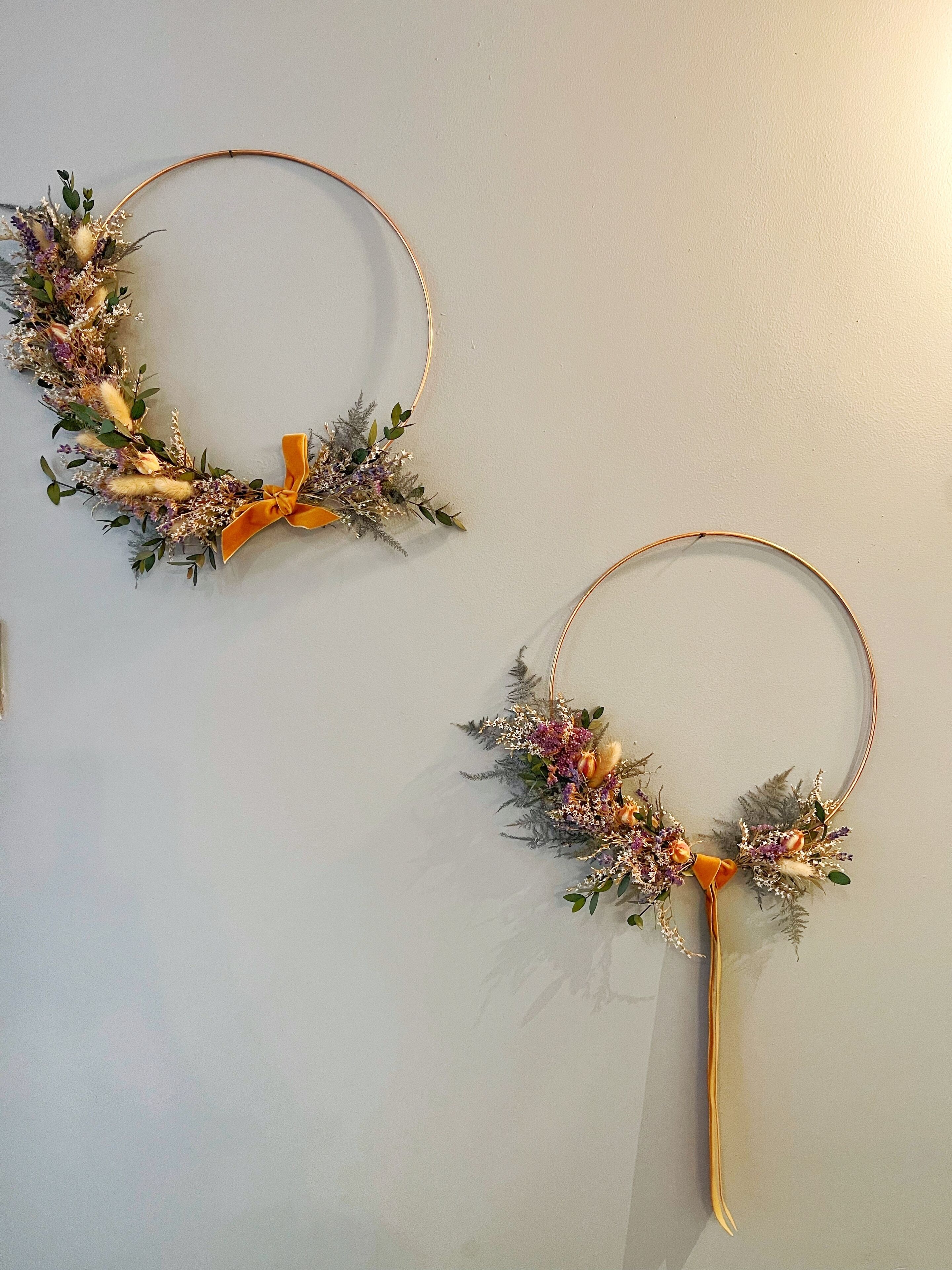 Two wall-mounted wreaths with floral arrangements and ribbons.