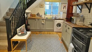 Een keuken met een vloerkleed met patroon, een wasmachine, een fornuis en een hanglamp.