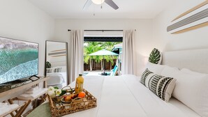 Ein Hotelzimmer mit Bett, Fernseher, Frühstückswagen und Blick auf Pool und Palmen.