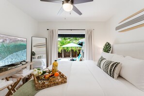 Ein Hotelzimmer mit Bett, Fernseher, Frühstückswagen und Blick auf Pool und Palmen.