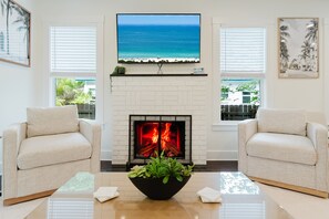 A living room with a fireplace, two sofas, a TV, and a view of the ocean.
