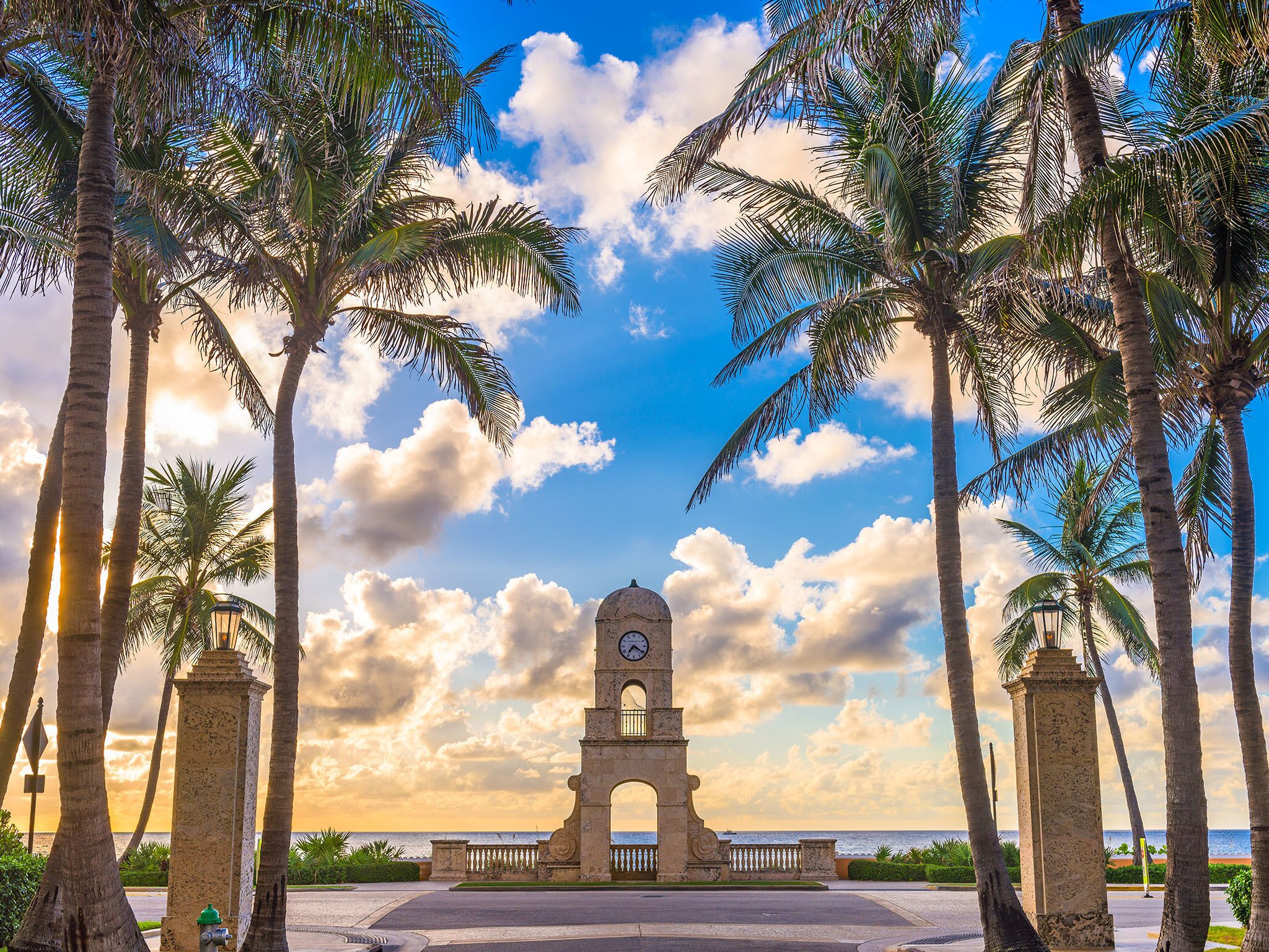 A historic clock tower with a clear view of the ocean, surrounded by palm trees.