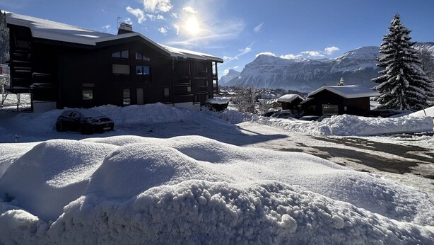 A snow-covered building with a mountain backdrop, a clear sky, and a sun shining.