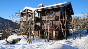 A multi-story building with balconies, surrounded by snow-covered ground and bare trees.